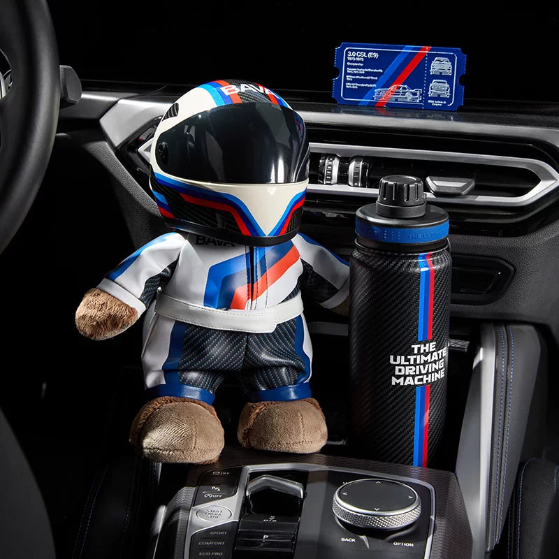 BMW M plush racer bear in helmet and racing suit with carbon-look Ultimate Driving Machine bottle in a BMW cockpit