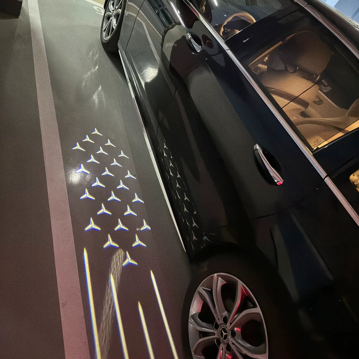 Shooting star welcome light pattern from the side mirror of a black Mercedes-Benz sedan