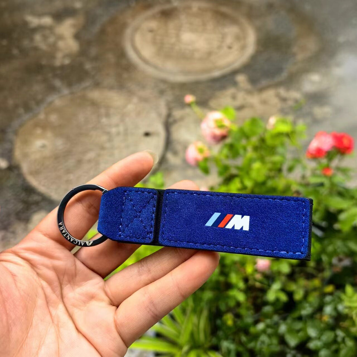 Blue Alcantara BMW M keychain with engraved metal key ring in hand