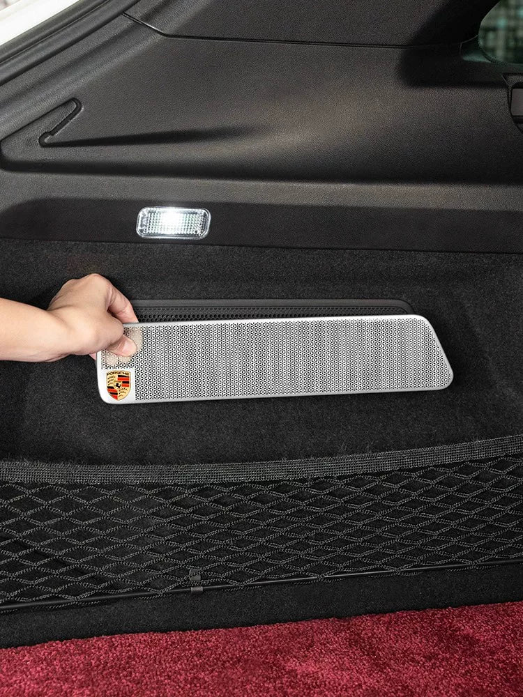 Silver trunk side speaker cover with Porsche crest being fitted in the Cayenne cargo area