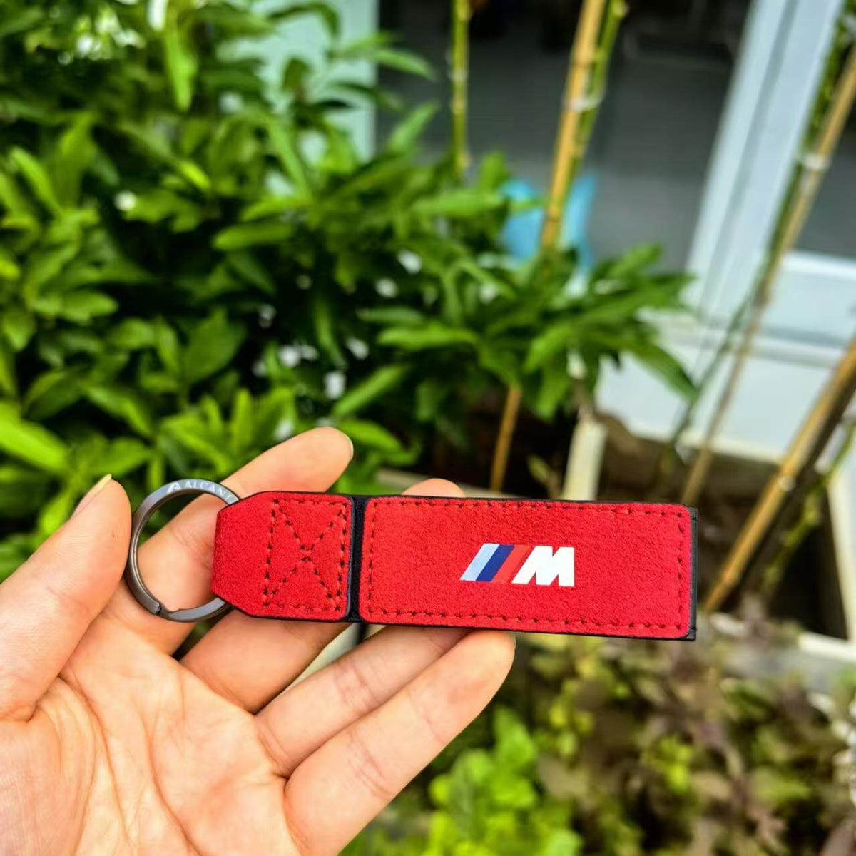 Red Alcantara BMW M suede keychain held in hand outdoors