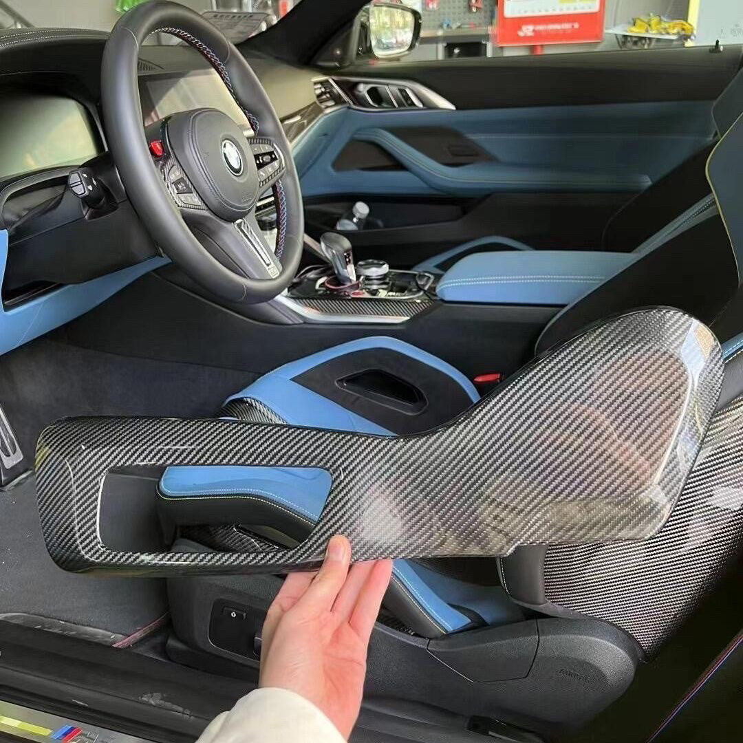 BMW M carbon fiber seat side panel held during installation, blue interior