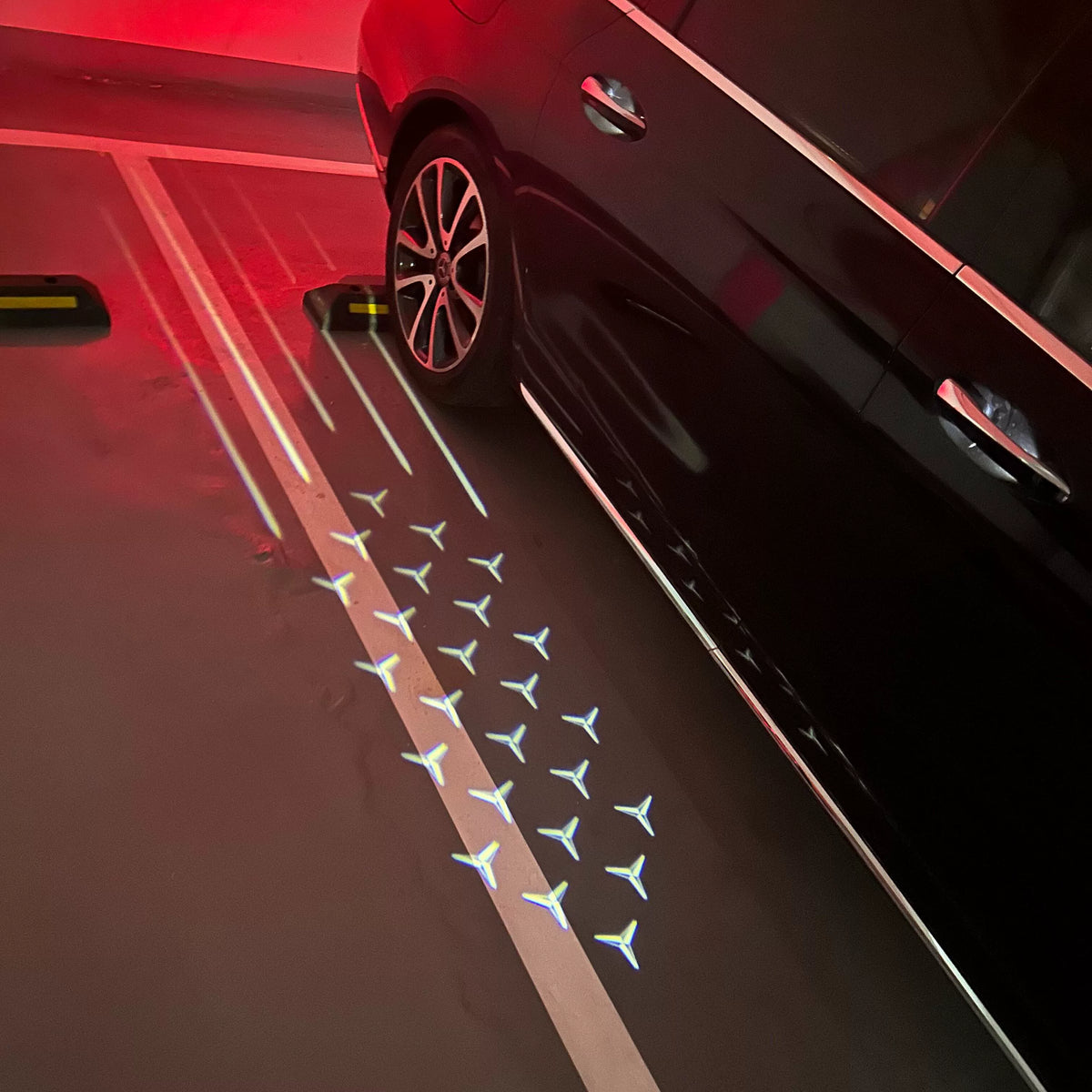 Mercedes-Benz Starfall mirror welcome light projecting stars and light trails beside a black Mercedes in a parking garage