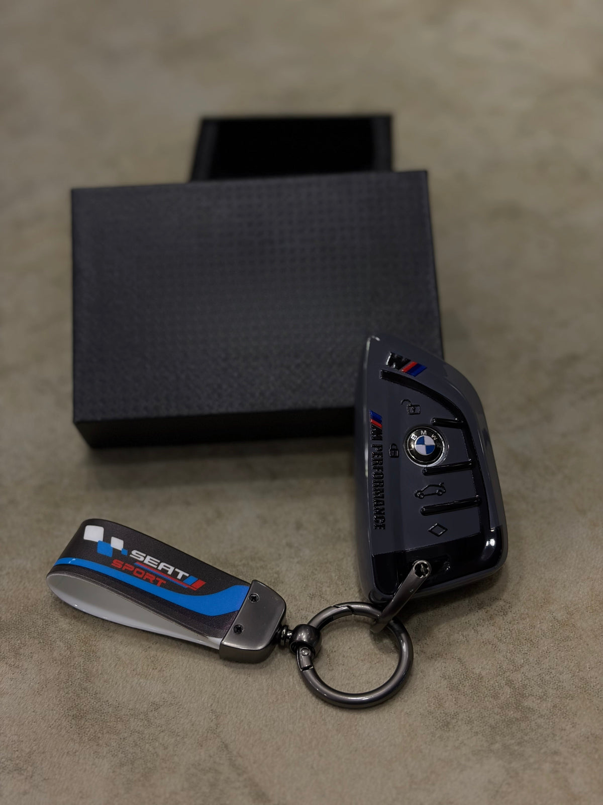 BMW M Performance grey key fob case with M Sport leather strap in front of black gift box