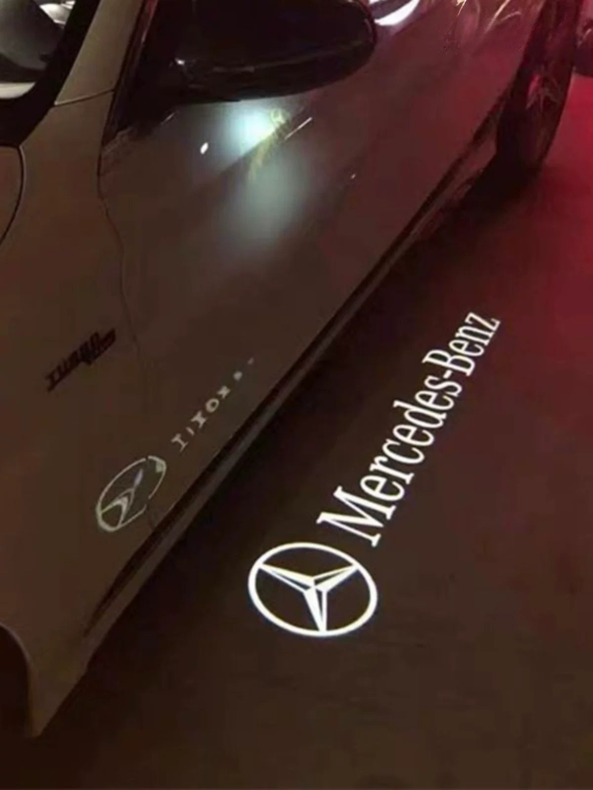 Mercedes-Benz star and wordmark light carpet projected from the side mirror at night