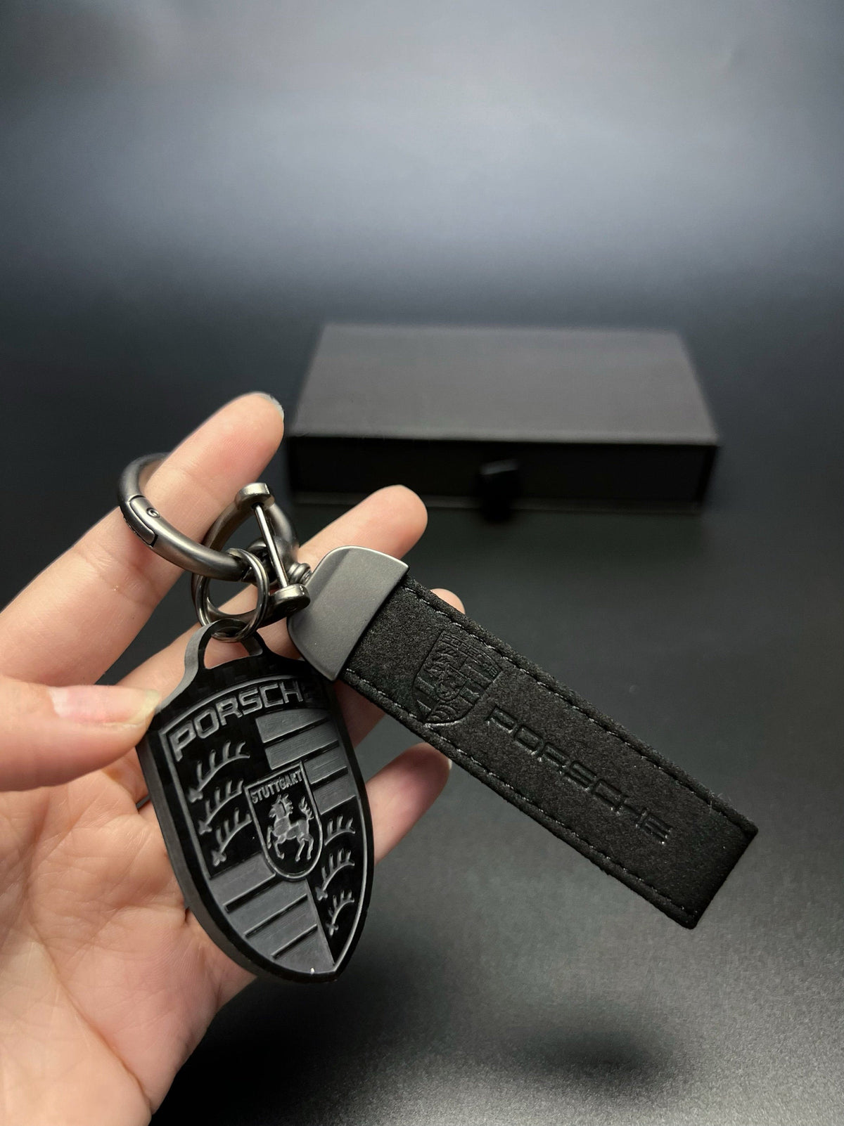 Porsche carbon fiber crest with black suede strap in hand